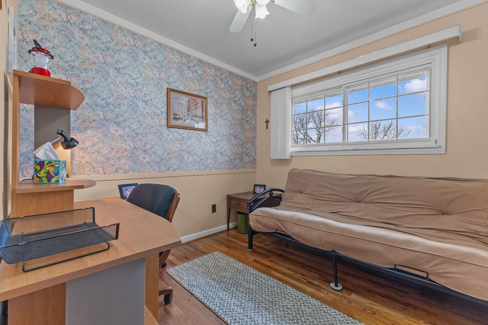 Cozy home office and sitting room with blue wallpaper, hardwood floors, futon, desk, and natural window light.