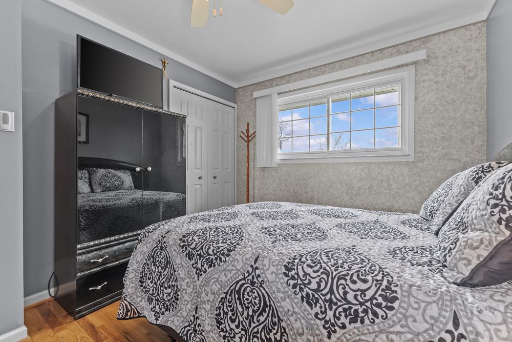 Cozy bedroom with black floral bedding, dark wood armoire with TV, white closet door, and bright window with wallpaper accent wall.