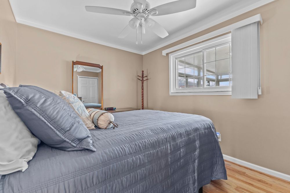 Cozy bedroom with blue bedding, hardwood floors, ceiling fan, and natural light from a large window.