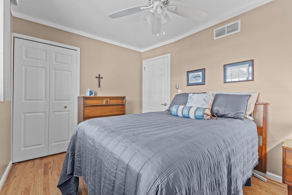 Bright bedroom featuring blue bedding, wood furniture, white closet doors, ceiling fan, and hardwood floors with crown molding.