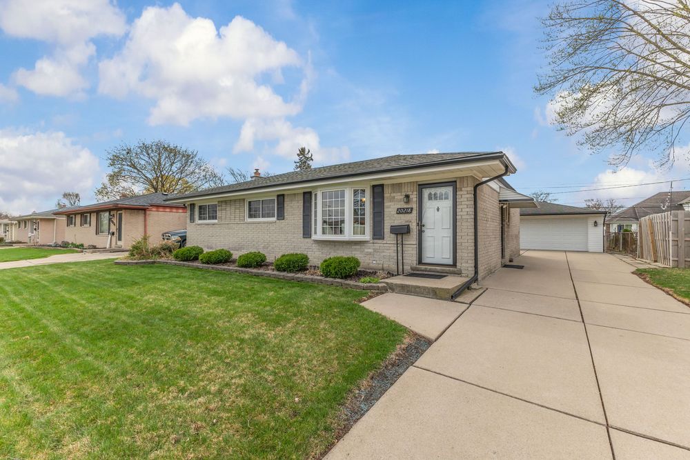 Charming brick ranch home with lush green lawn, attached garage, and welcoming front entrance on a sunny spring day.