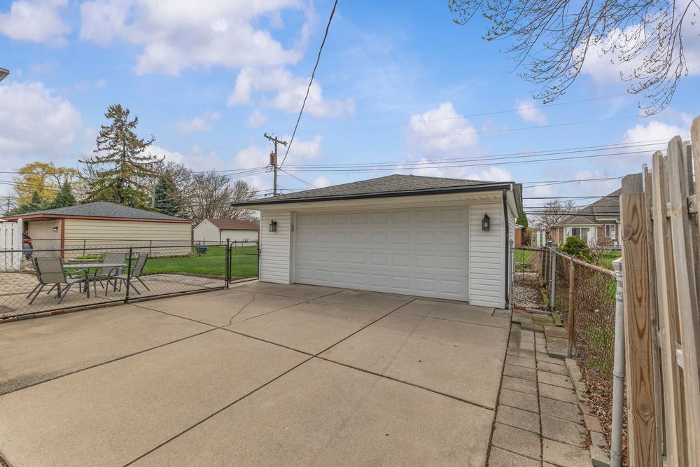 Detached two-car garage with white doors and concrete driveway in a residential backyard on a partly cloudy day.