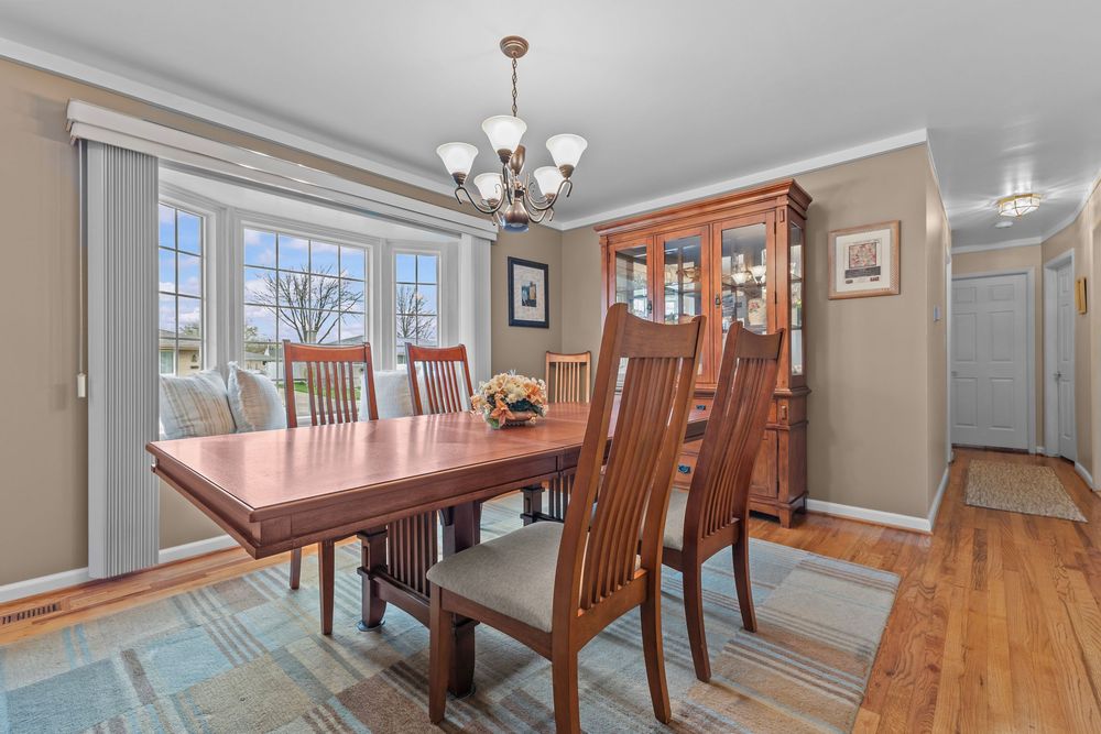 Elegant dining room with hardwood floors, Mission-style table and chairs, china cabinet, chandelier, and bay window with natural light.