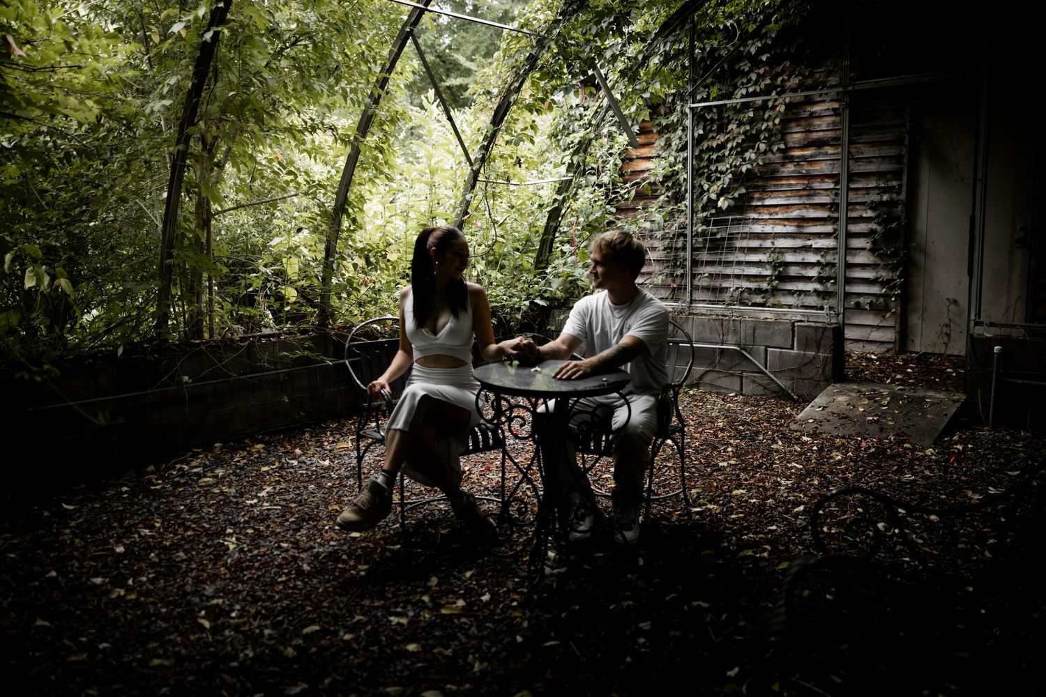 Groom in gray suit embracing bride in white dress among trees with fairy lights.