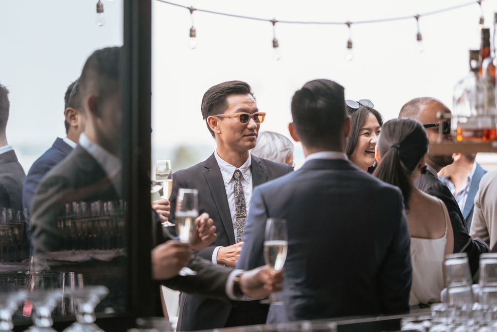 Guests in formal attire socializing at an outdoor rooftop wedding reception with champagne glasses.
