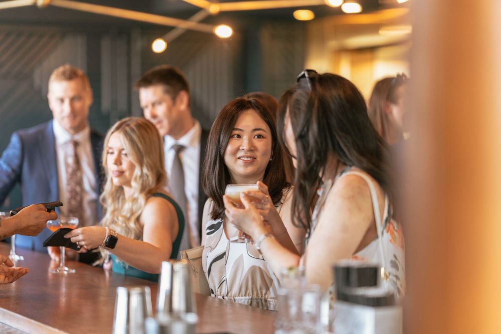 Women socializing at a bar, smiling and holding drinks at an elegant indoor venue.