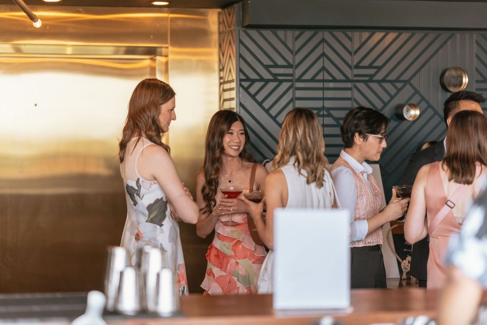 Guests socializing at an elegant indoor cocktail party, holding drinks near a gold elevator and geometric wall decor.