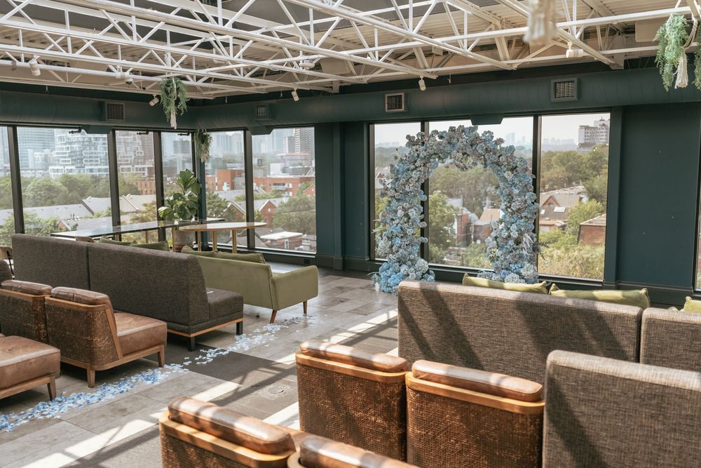 Modern rooftop lounge with green walls, brown leather chairs, large windows, and a floral arch centerpiece.