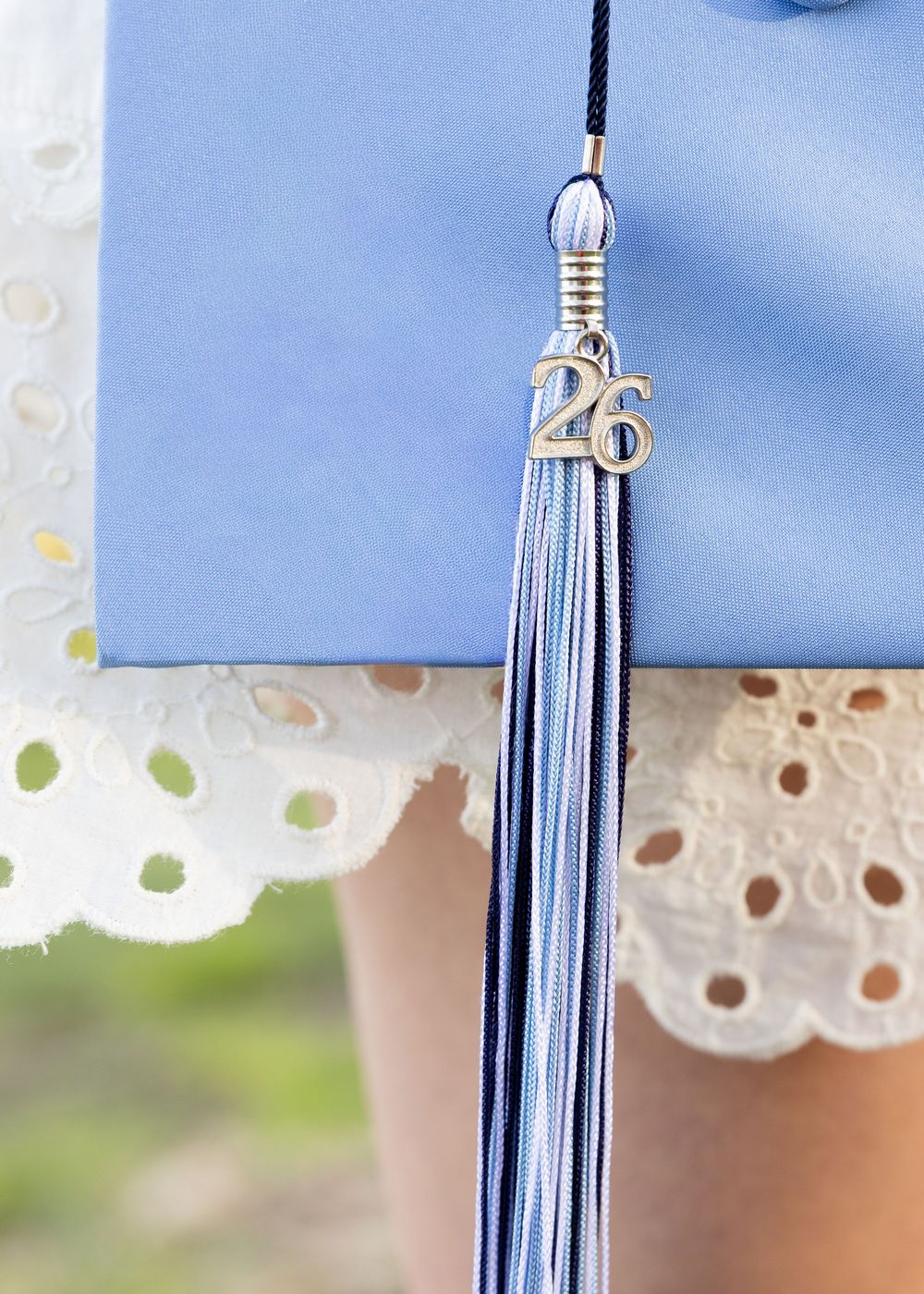 Close-up of light blue graduation cap with class of 2026 tassel charm on white lace dress.
