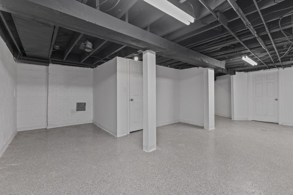 Spacious unfinished basement with white walls, concrete floor, support column, and exposed ceiling joists. Detroit MI Real Estate Photograph