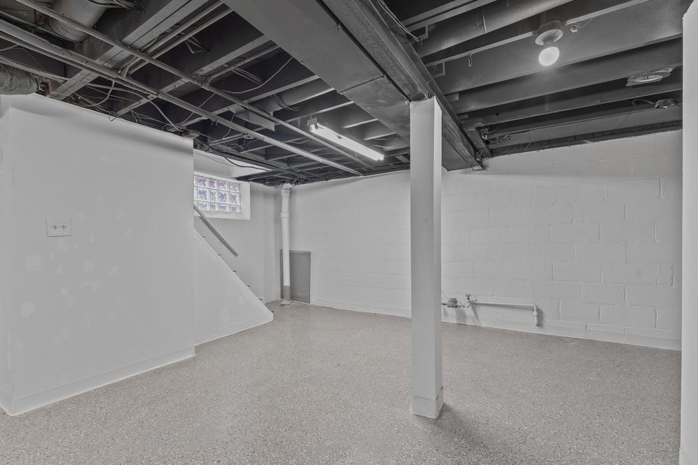 Unfinished basement with exposed ceiling joists, painted white concrete walls, epoxy floors, and a support column. Detroit MI Real Estate