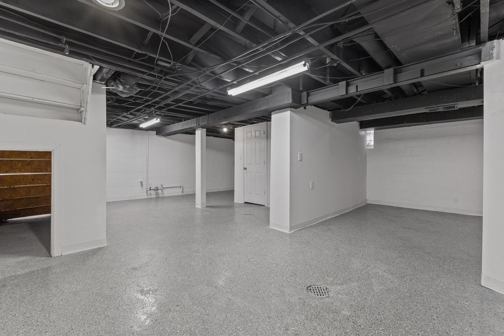 Spacious commercial basement with polished concrete floors, white walls, exposed black ceiling, and fluorescent lighting. Detroit MI Real