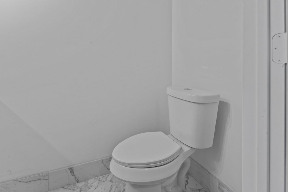 Simple white toilet in a small basement bathroom with marble tile flooring.