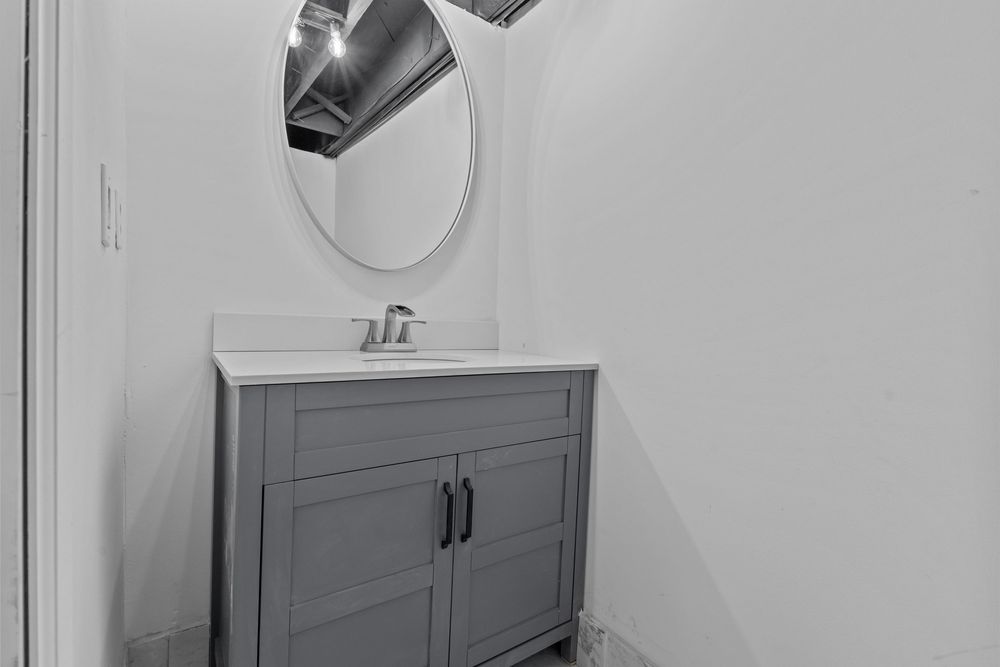 Gray bathroom vanity with white countertop, round mirror, and black hardware in a clean modern bathroom.