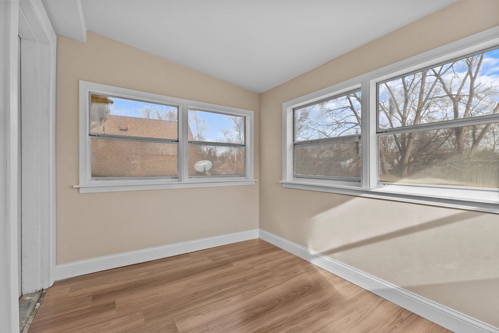 Bright empty room with light wood floors, white trim, and two large windows overlooking bare trees. Detroit MI Real Estate Photographer