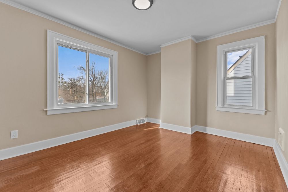 Bright empty room with hardwood floors, crown molding, and two windows allowing natural light. Detroit MI Real Estate Photographer