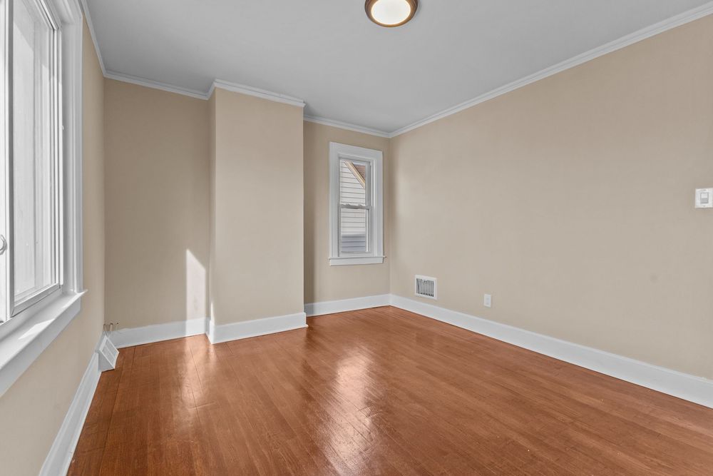 Bright empty room with hardwood floors, crown molding, and two windows allowing natural light in a residential home. Detroit MI Real Estate