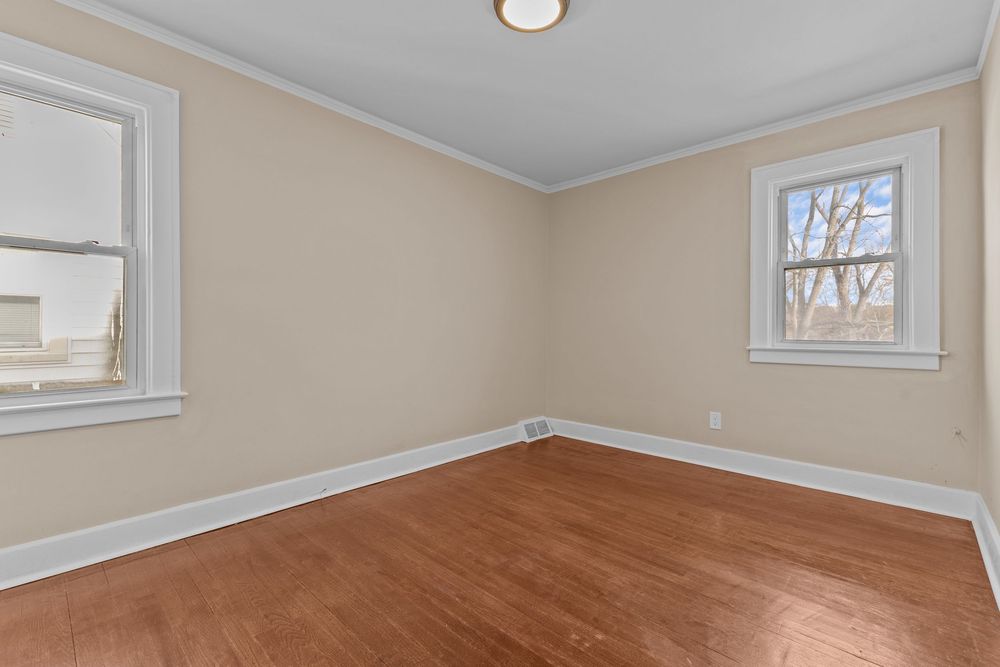 Spacious empty bedroom with rich hardwood floors, crown molding, and two windows with natural light. Detroit MI Real Estate Photograph
