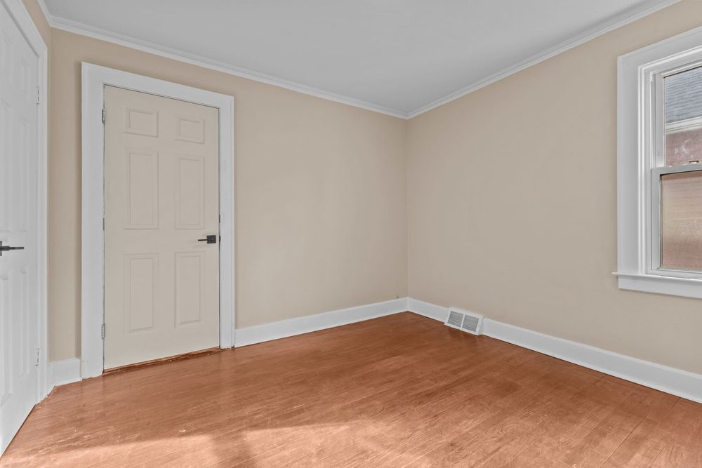 Empty room with light hardwood floors, crown molding, white door, and a bright window.
