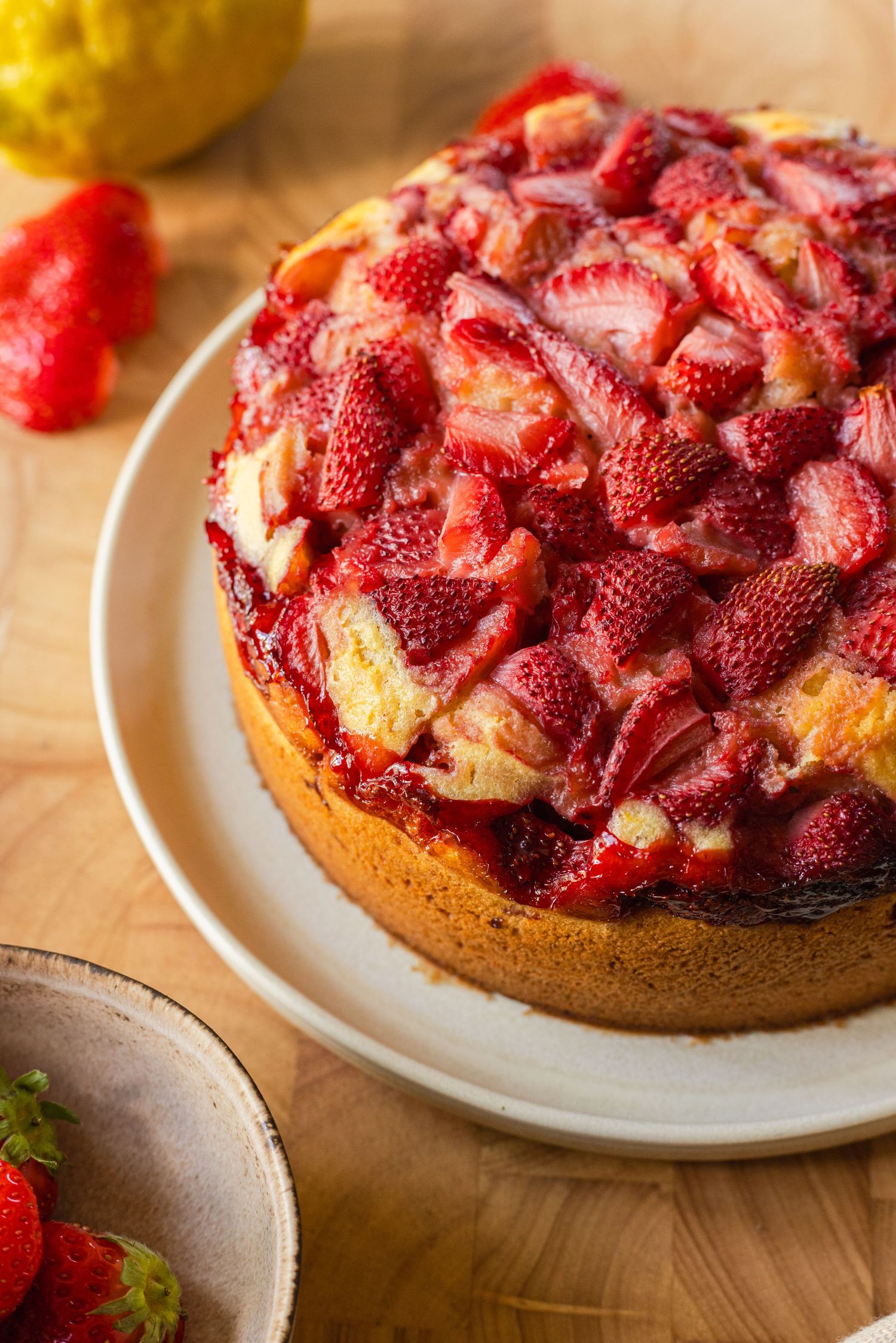 Homemade strawberry upside-down cake topped with fresh sliced strawberries on a white plate on a wooden table.