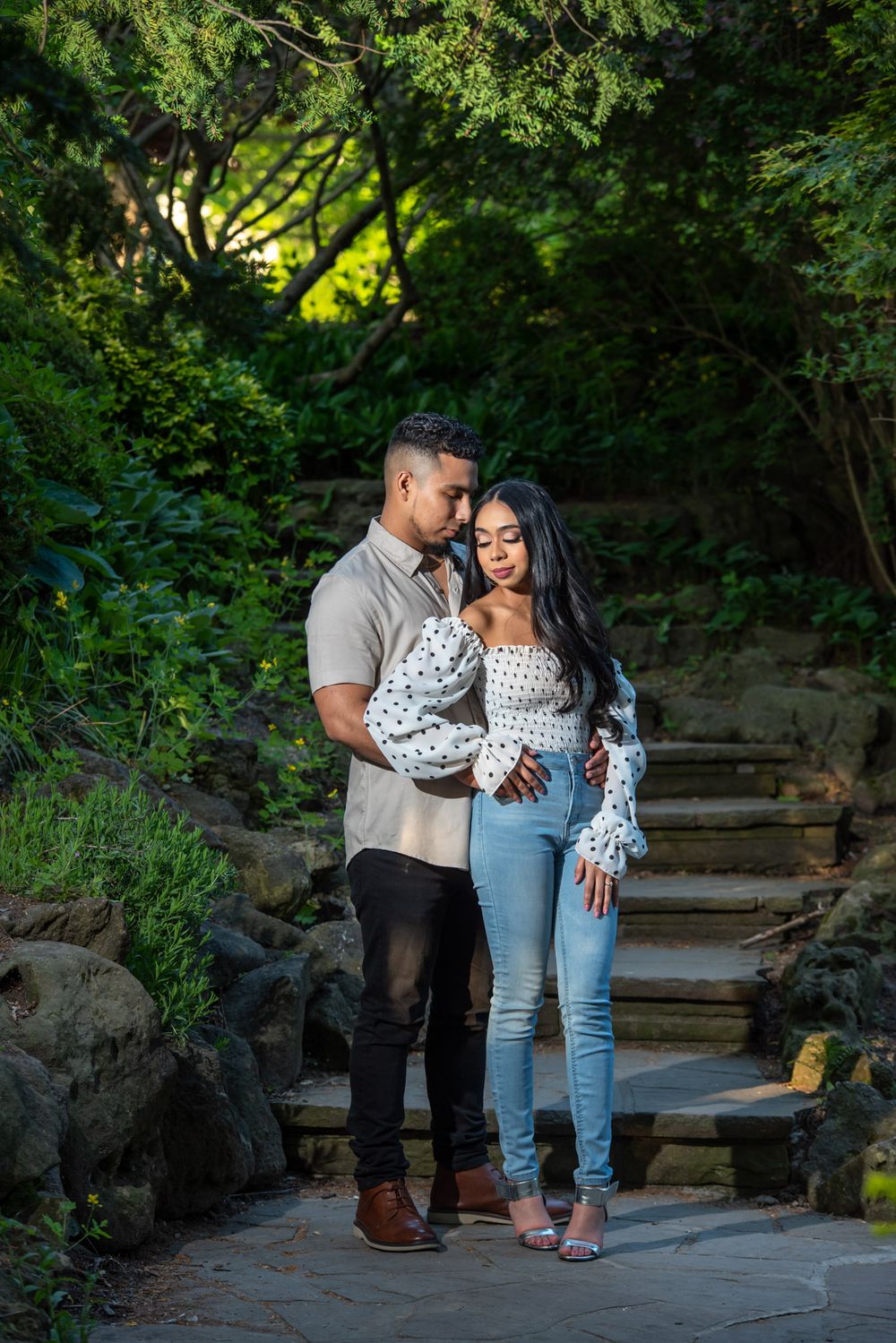 Couple embracing on a garden path surrounded by lush greenery and stone steps.