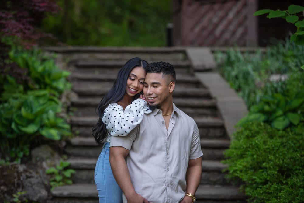 Couple sharing a tender embrace in front of stone steps surrounded by vibrant green garden plants.
