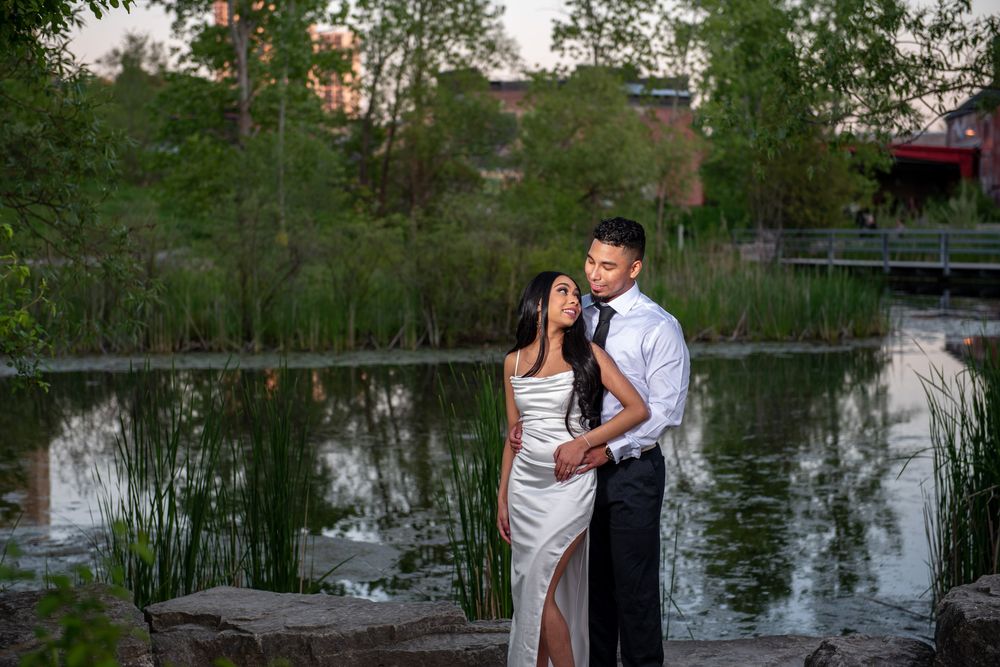 Elegant couple in formal wear embracing by a tranquil pond at dusk.