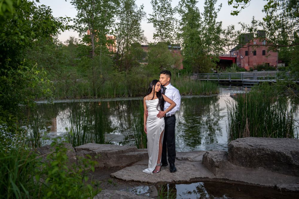 Couple posing romantically on rocks by a pond with a pink building in background.