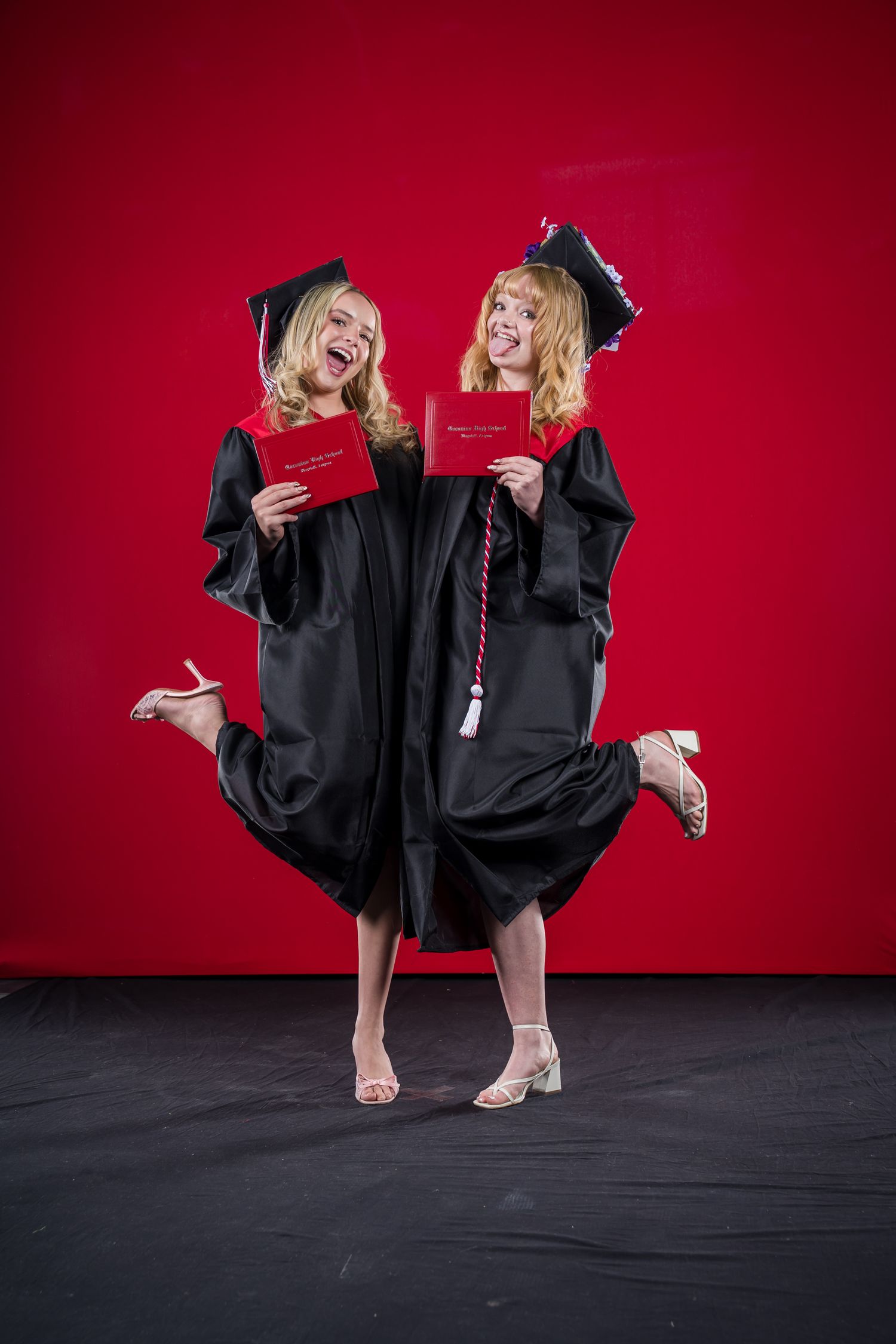 2025 CHS graduate in black cap and gown poses energetically against a bright red backdrop during commencement photo session.
