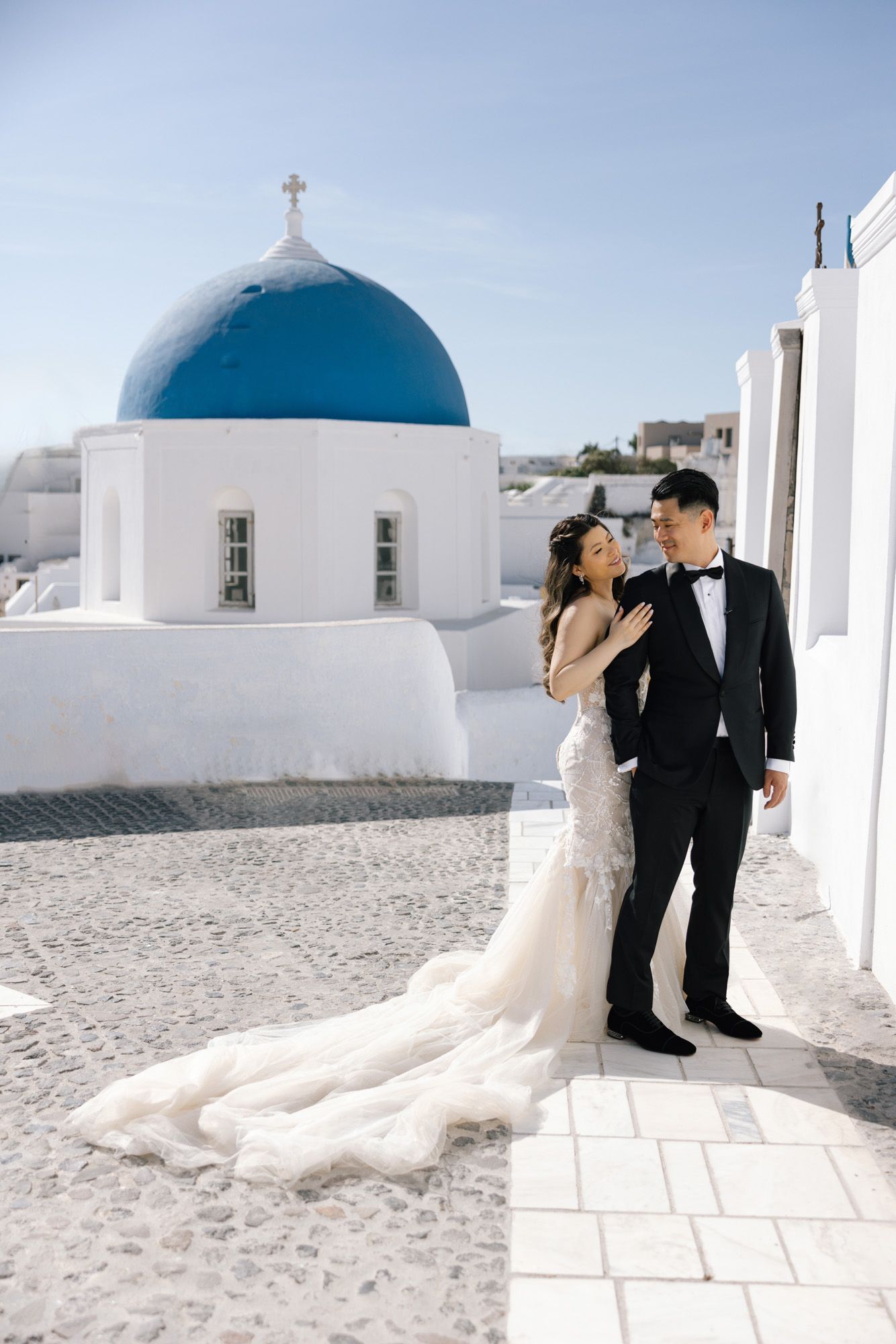 Bride in flowing white gown poses near fountain outside French chateau.