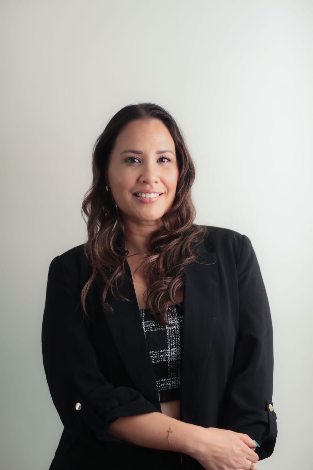 Professional woman in black blazer smiling confidently with arms crossed against a light background.