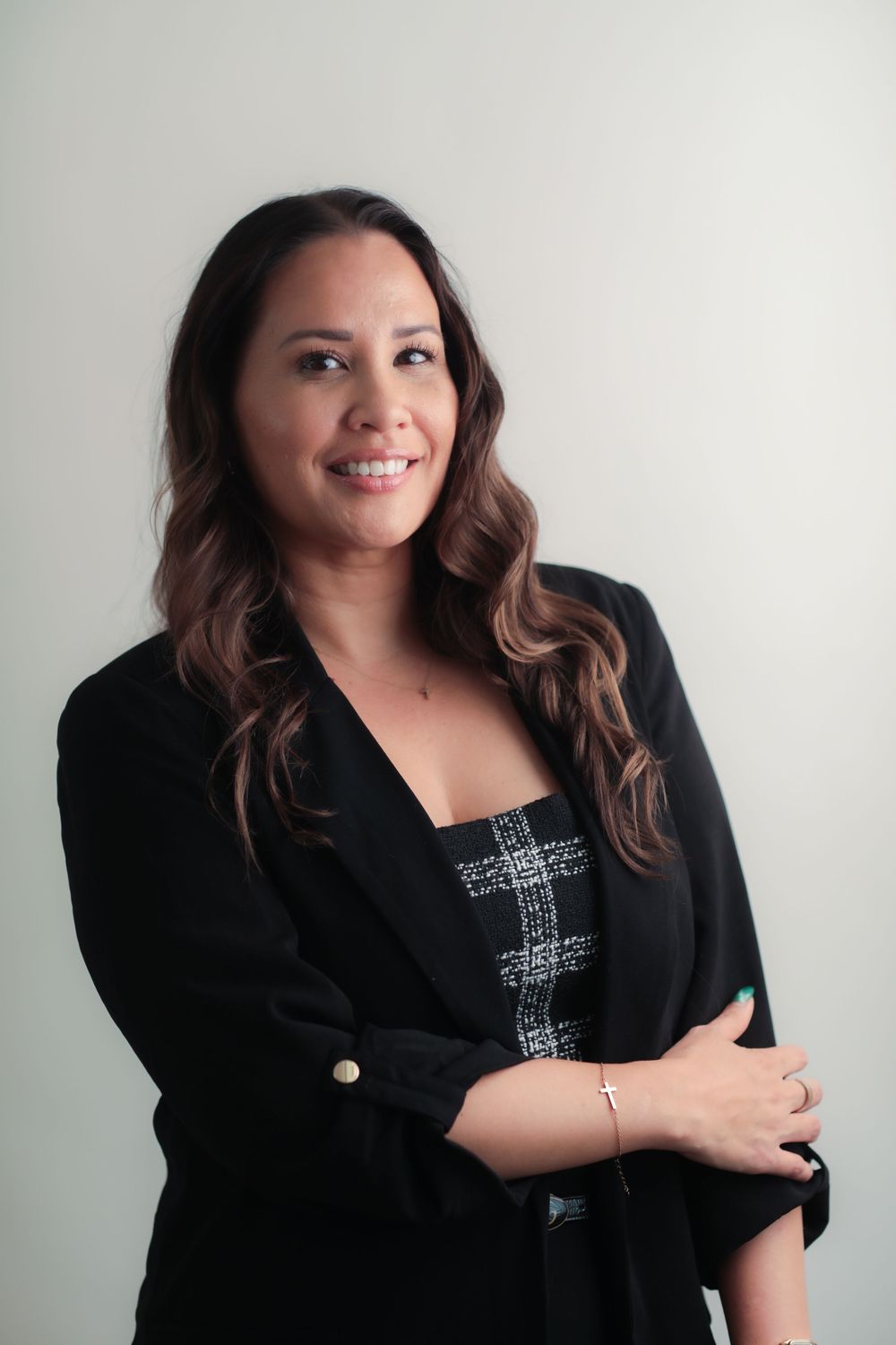 Professional woman in black blazer smiling confidently with arms crossed against a light gray background.