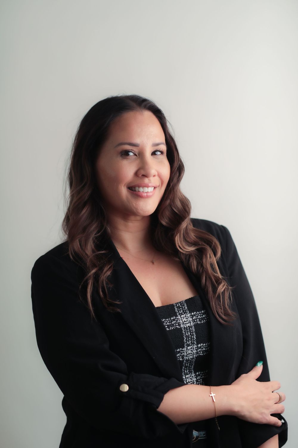 Professional woman in black blazer smiling confidently with arms crossed against a light gray background.
