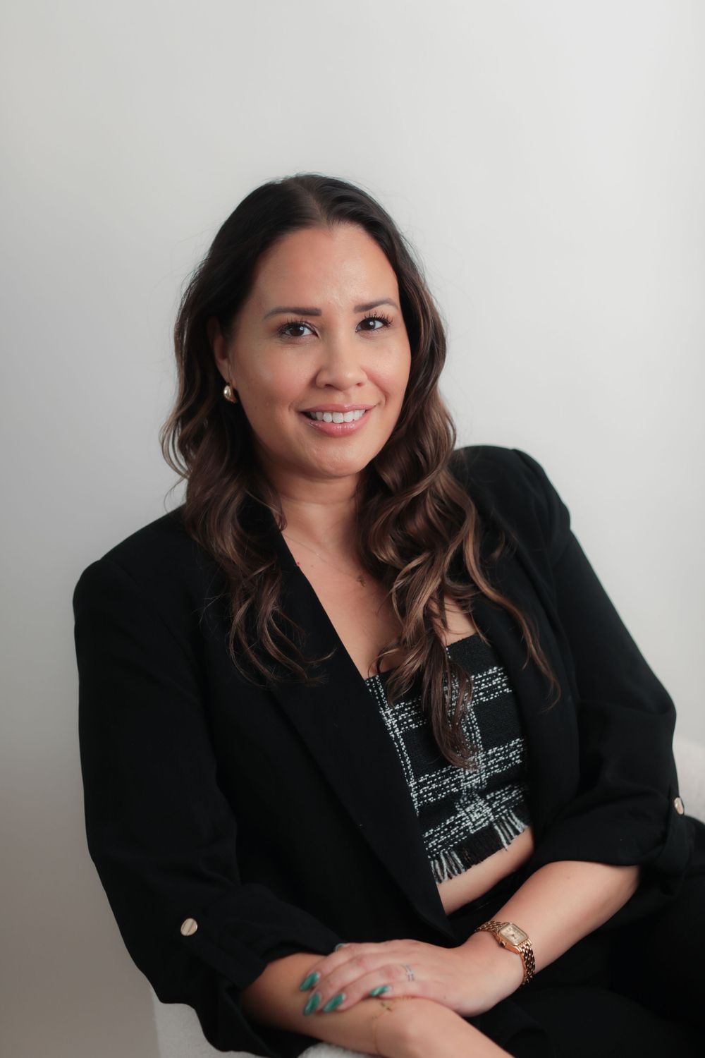 Professional woman in black blazer and patterned top smiling confidently in a modern studio setting.