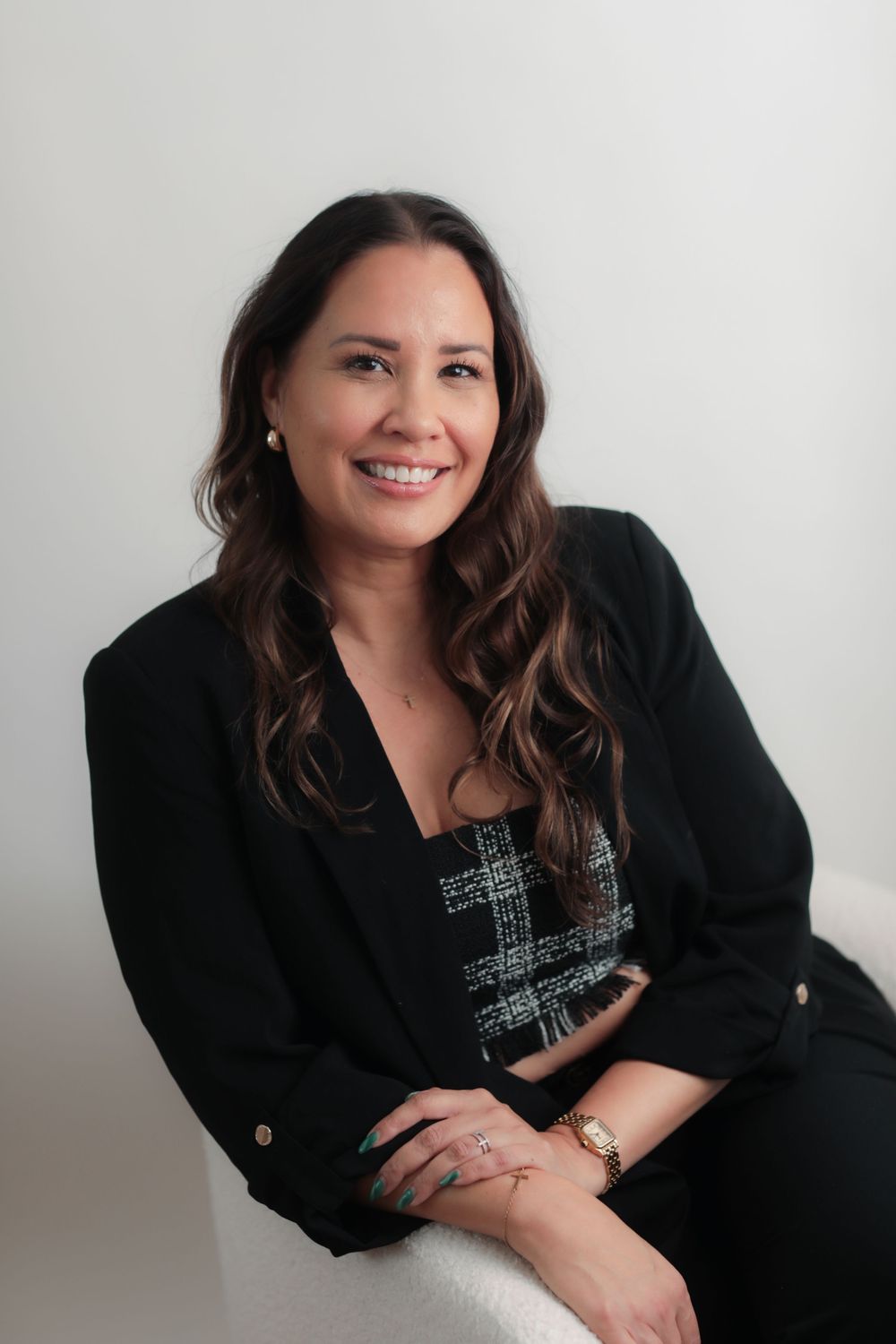 Professional woman in black blazer and plaid top smiling confidently against white background.