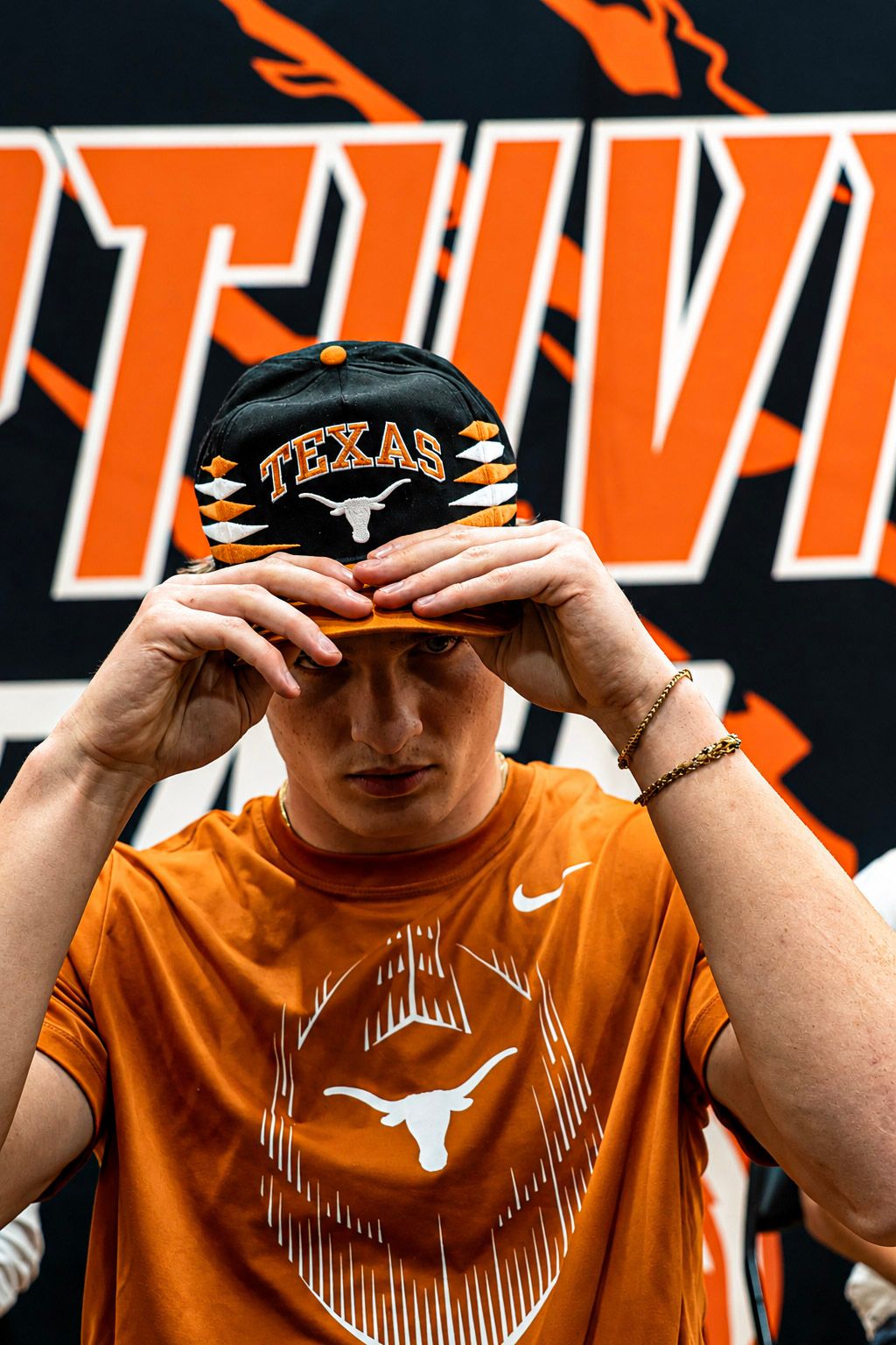 A young man in a Texas Longhorns orange Nike shirt adjusts a Texas Longhorns snapback hat at a signing event.