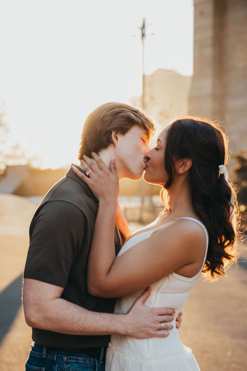 Couple sharing a romantic sunset kiss outdoors, golden backlight glowing behind them.