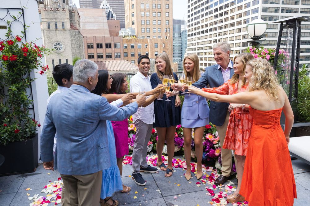 Group of friends toasting with champagne glasses on a flower-decorated rooftop in the city.