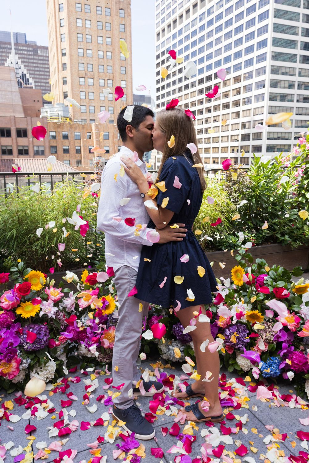 Couple kissing on a rooftop as colorful flower petals rain down around them.