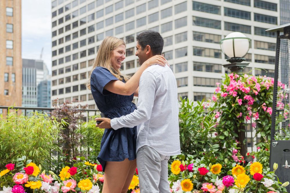 Smiling couple embracing on a rooftop terrace surrounded by vibrant blooming flowers.
