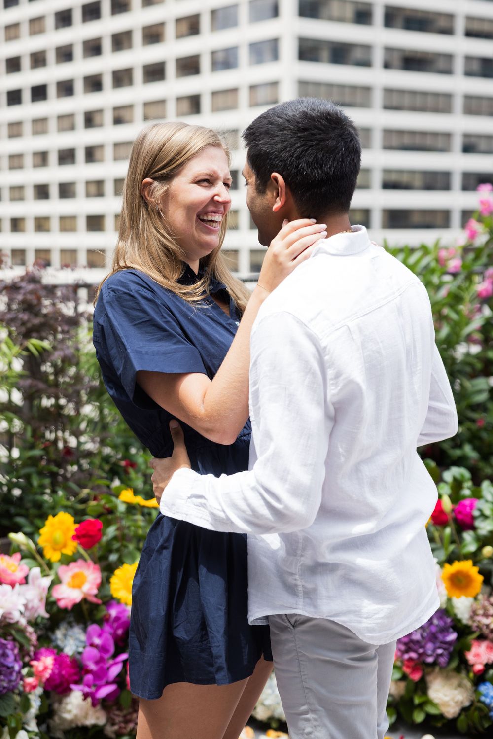 Joyful couple embracing and laughing on a rooftop garden surrounded by colorful flowers.