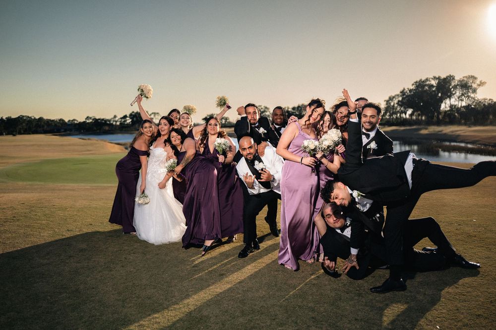 Wedding party in purple dresses and tuxedos posing playfully on a golf course at golden hour.