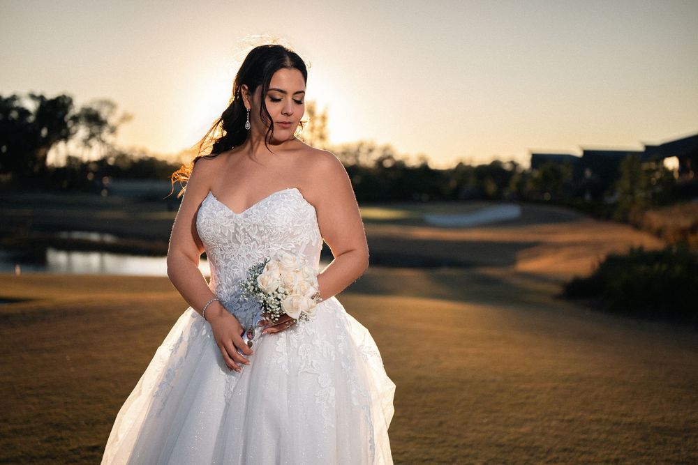 Bride in strapless white ball gown holding bouquet at golden sunset on golf course.