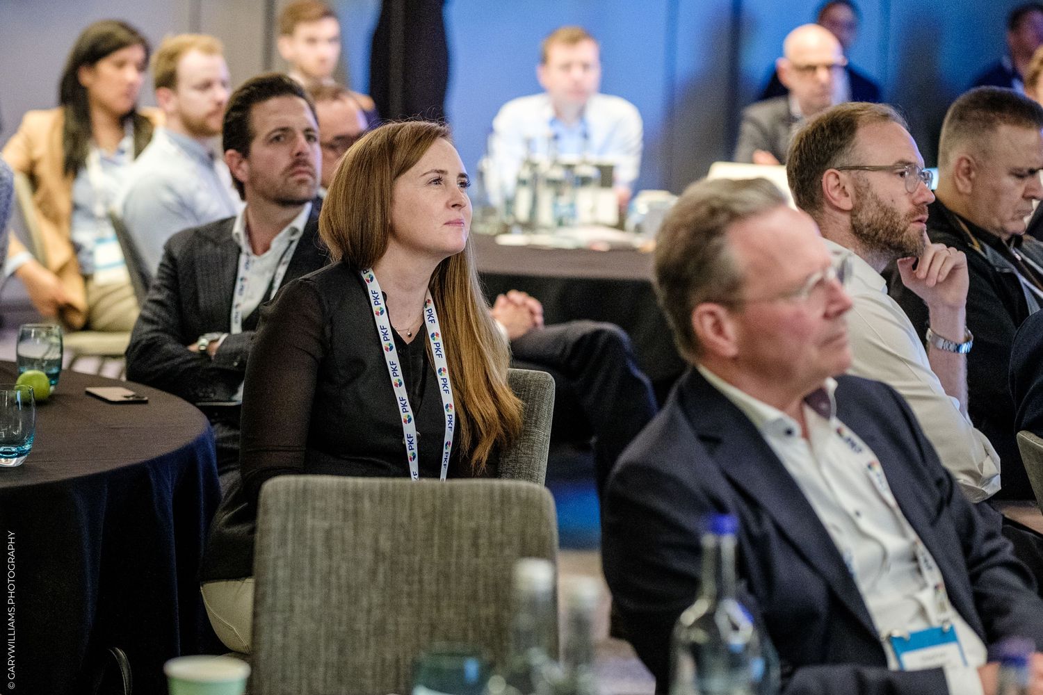 Professionals attentively listening at a corporate conference, seated in rows with water bottles on tables.
