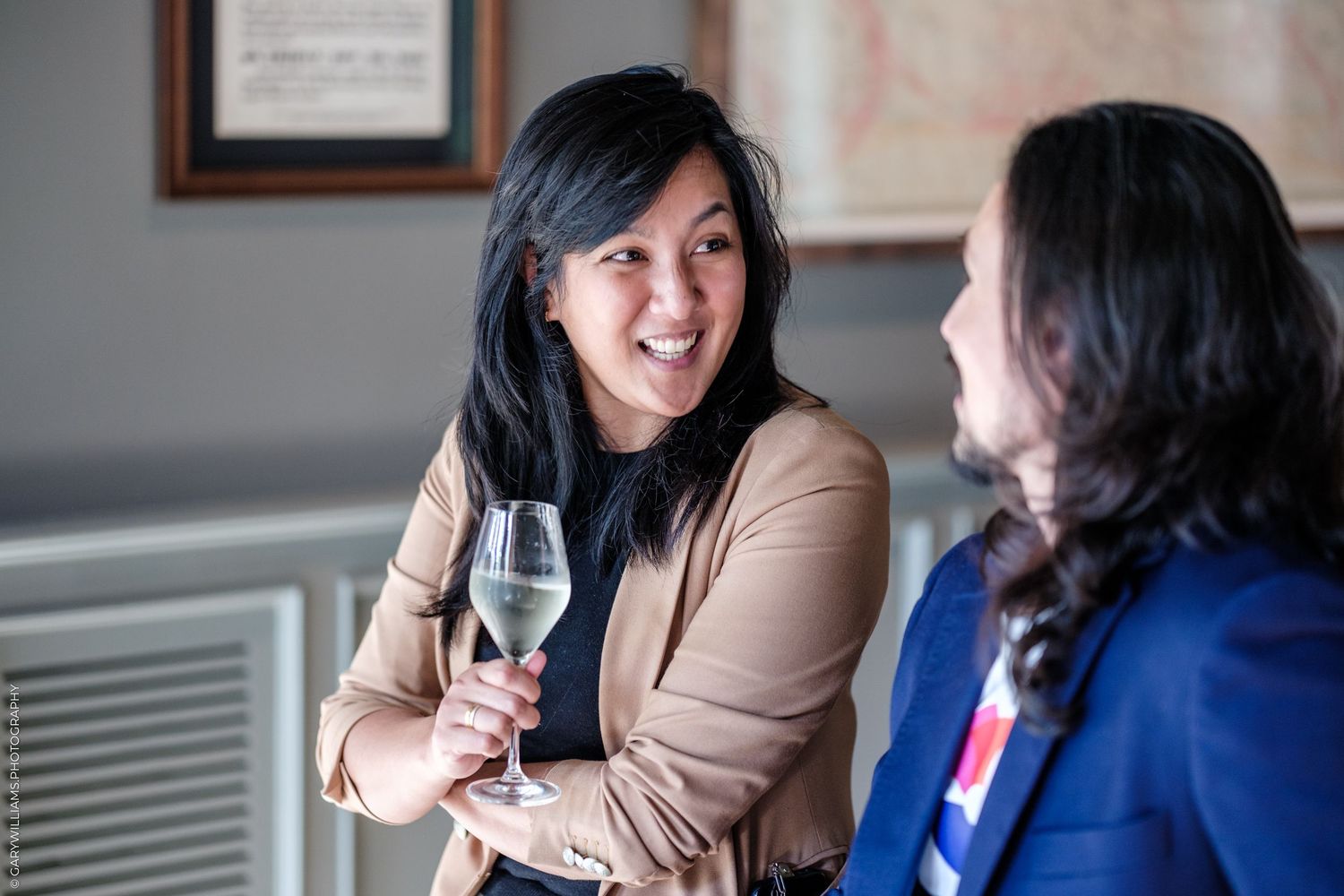 Two women networking at a social event, one holding a glass of white wine, smiling and engaged in conversation.