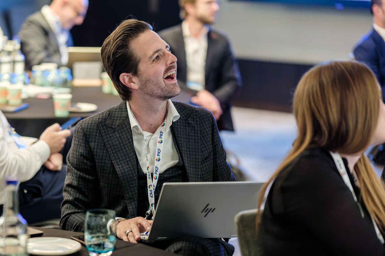 Man in blazer laughing at conference table with HP laptop, engaging in lively business networking event discussion.