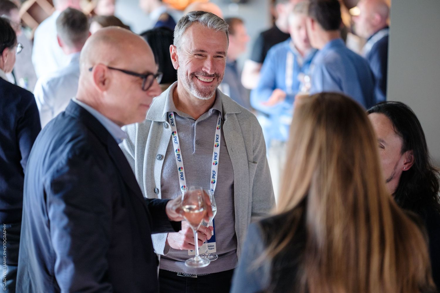 Professionals networking at a business conference, smiling and holding drinks in a modern venue.