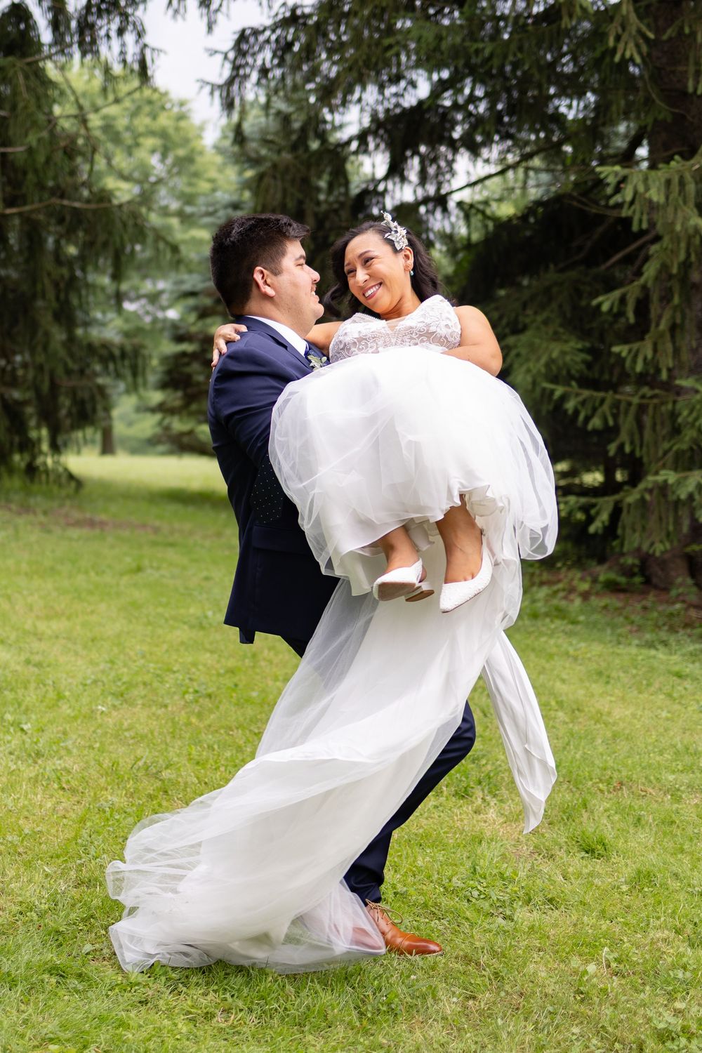 Groom in navy suit carrying smiling bride in white wedding gown outdoors Eden Park. Cincinnati Elopement Photo