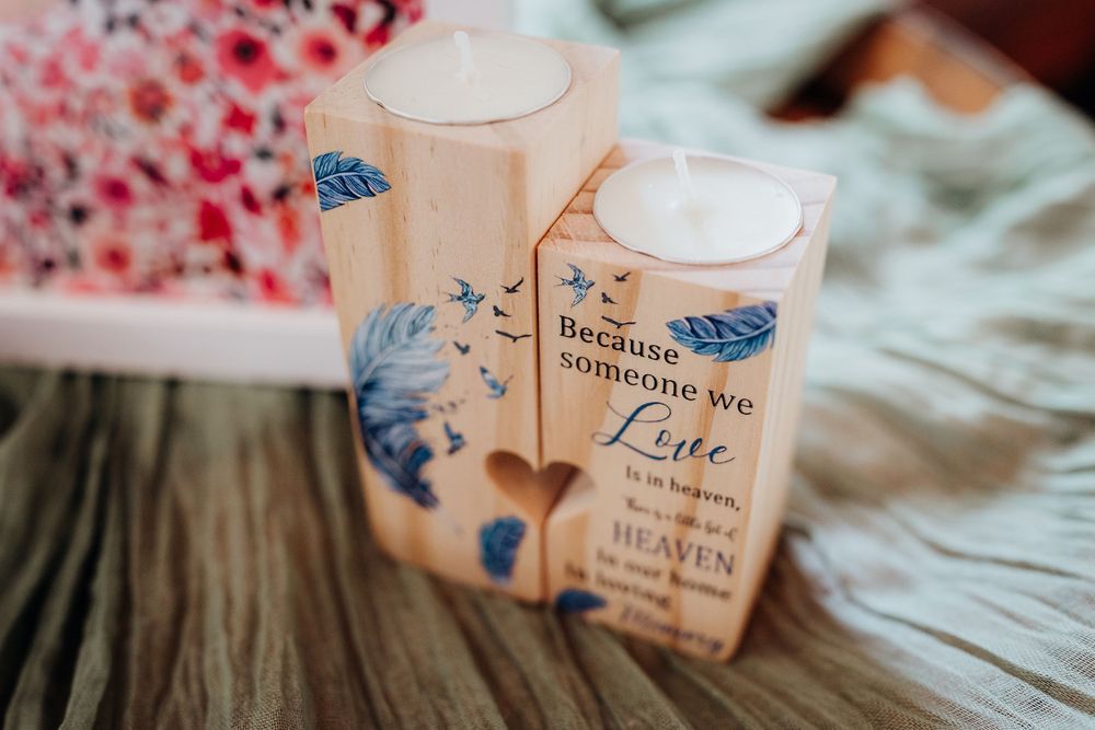 Wooden candle holders with blue feather design and memorial quote about love and heaven, displayed on a cozy surface.