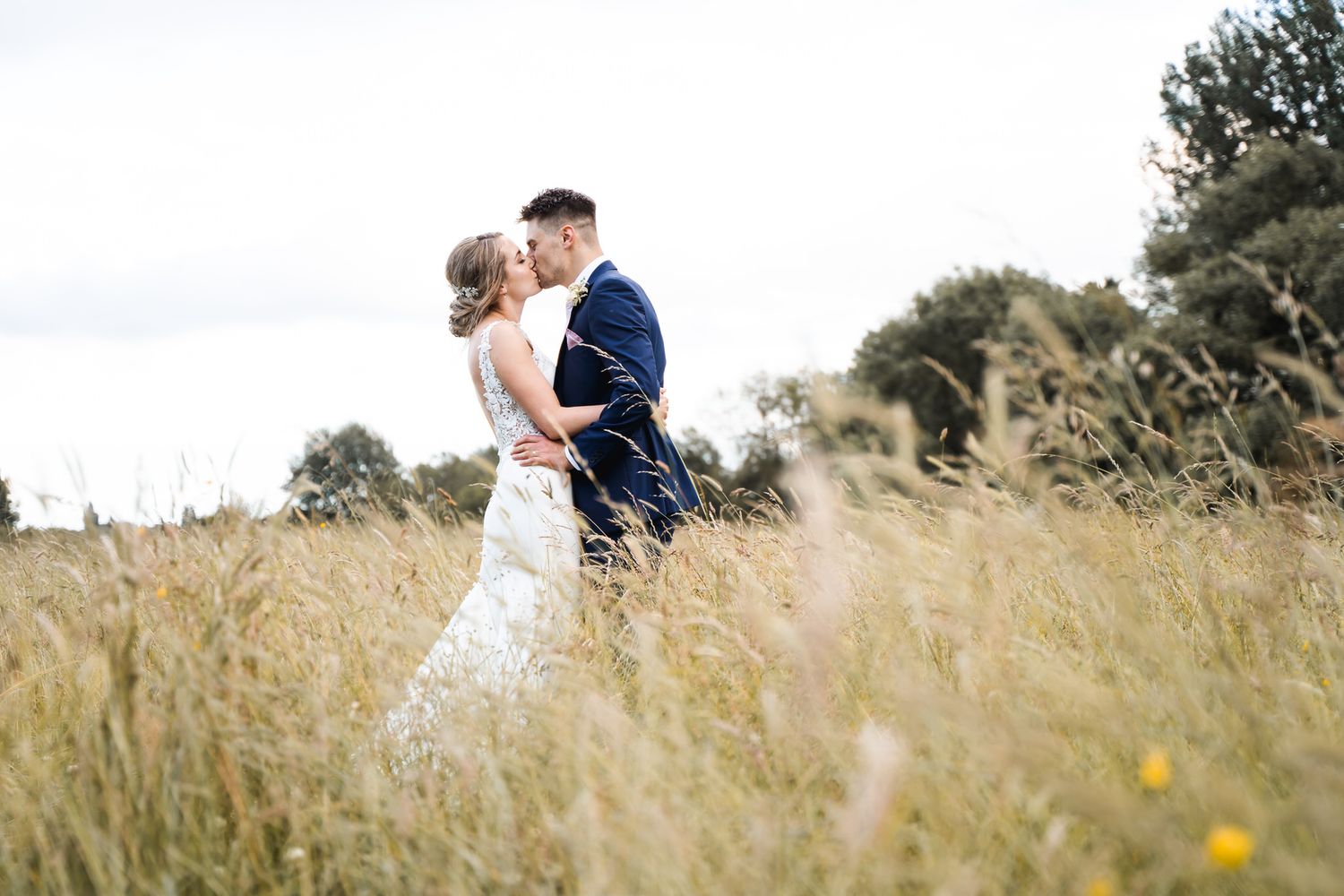 Bride and groom sharing a kiss in front of a rustic wooden barn surrounded by lush greenery on their wedding day.